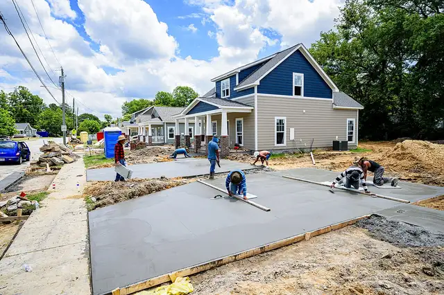 Crew finishing fresh concrete slabs in front of new homes